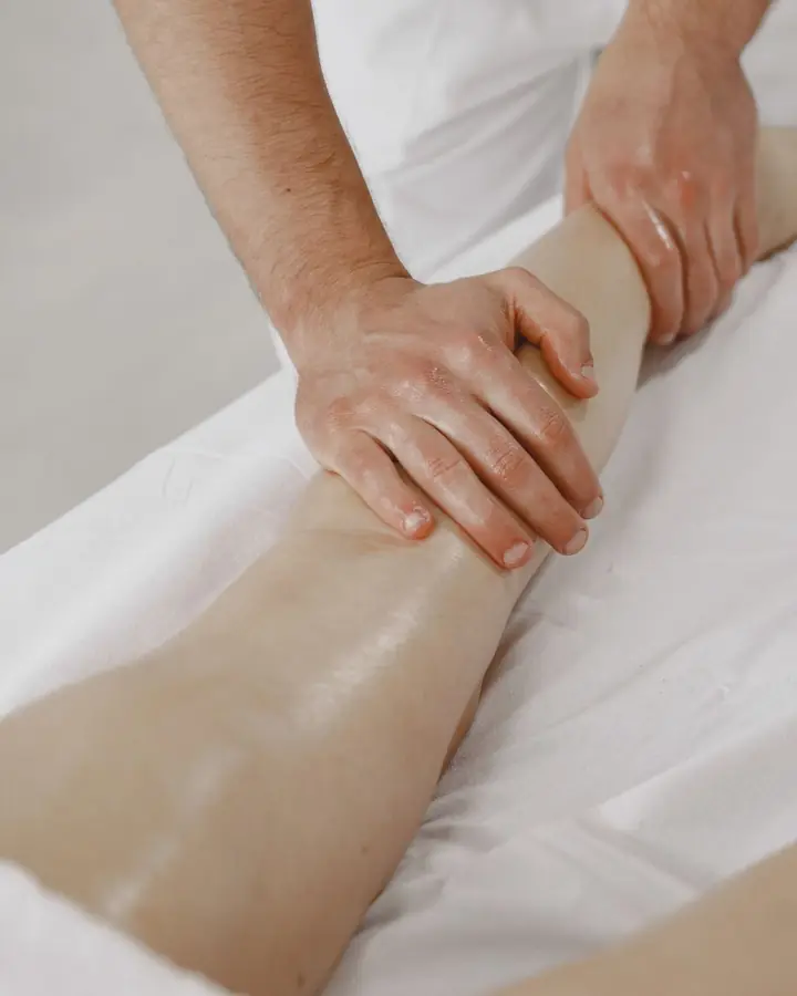 Hands working along the lower leg on a treatment table