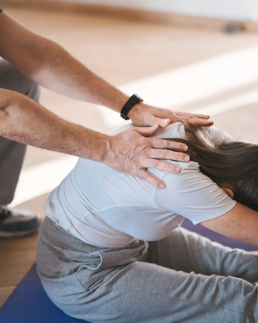 A practitioner's hands guiding a seated client's shoulders into a forward-fold stretch